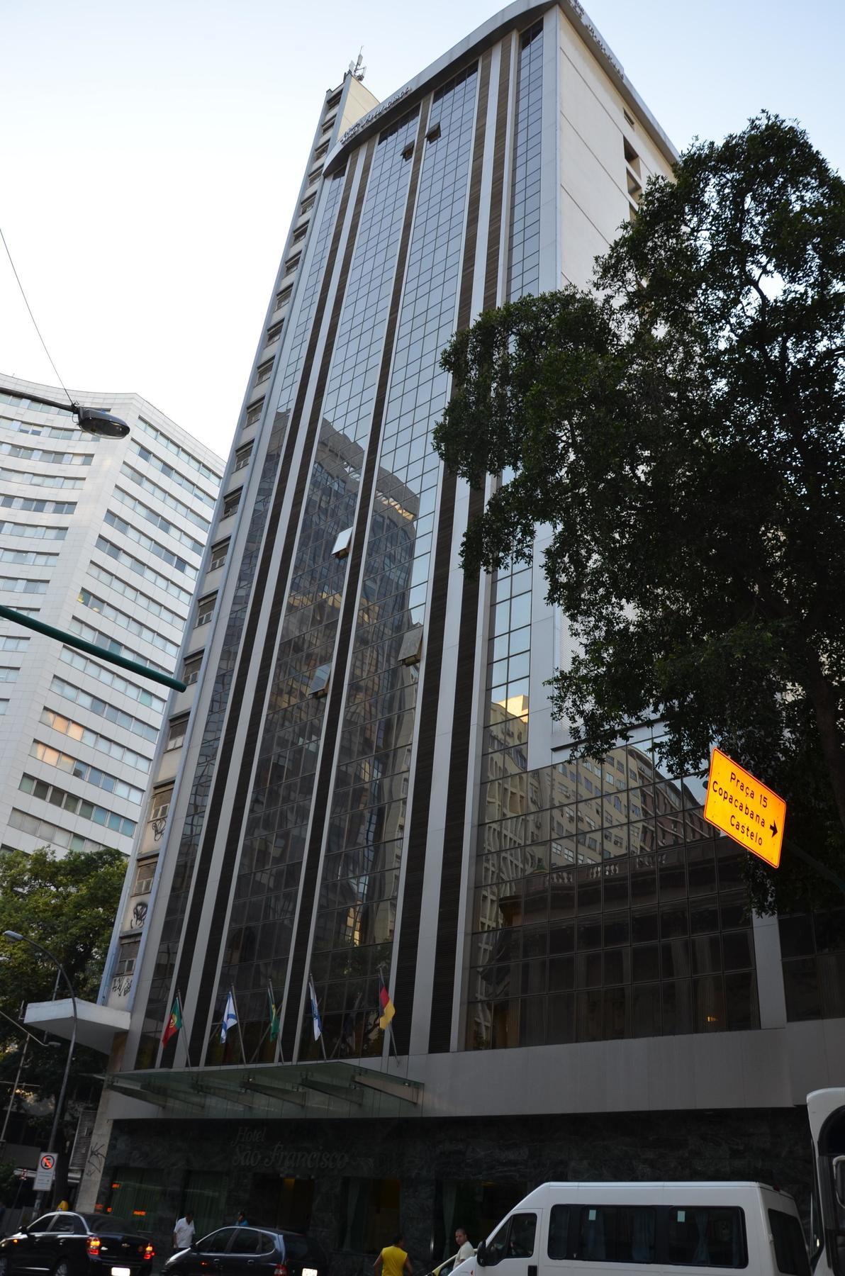 Hotel Atlantico Tower Rio de Janeiro Exteriör bild The photo shows a city street with tall buildings. In the foreground, there is a modern glass skyscraper featuring reflective surfaces and vertical lines. Next to it, there's another building with a different architectural style, also made of glass. 